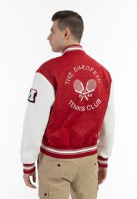 Giacca varsity rossa e bianca con colletto e polsini a coste, caratterizzata da testo "THE EUROPEAN TENNIS CLUB" e grafica di una racchetta da tennis sul retro.
