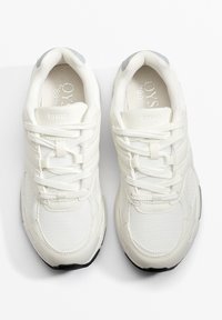 Białe sportowe sneakersy z połączeniem gładkiej skóry i siateczki. Wyściełany kołnierz z szarymi akcentami, płaskie sznurowadła i czarna gumowa podeszwa.