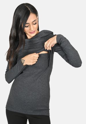 Top grigio a maniche lunghe con un design drappeggiato e un'apertura laterale. Il materiale sembra morbido con una texture liscia. Abbinato a pantaloni scuri aderenti.