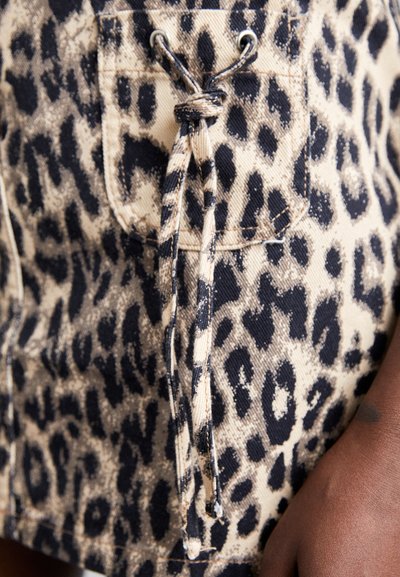 Leopardmønstret stoff med en beige bakgrunn, med en frontlomme, metalløye og en bundet snor for justering. Myk tekstur.