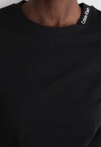 Sort bomulds T-shirt med rund halsudskæring. Har et hvidt "Calvin Klein" mærke på kraven. Glat tekstur, korte ærmer.