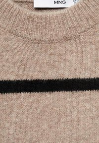 Pull en maille beige avec un col côtelé et une bande noire horizontale au niveau de la poitrine.