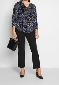 Svart blus med blå och vita blommönster, krage och trekvartslånga ärmar, ihop med svarta utsvängda byxor och en liten svart handväska.