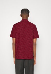 Camisa de manga corta con un patrón rojo sobre un fondo oscuro, con dobladillo recto y cuello. Fabricada con un tejido ligero.