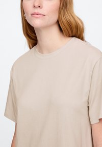 Béžové bavlnené tričko s krátkymi rukávmi a okrúhlym výstrihom, s hladkou textúrou a uvoľneným strihom. Bez viditeľných vzorov alebo ozdôb.