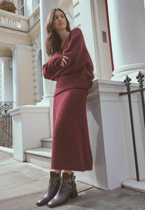 Pull en maille bordeaux associé à une jupe midi au toucher doux. Bottines noires à la cheville avec des accessoires en argent et des bouts pointus.