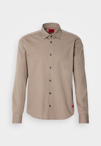 Camisa de botón de manga larga beige con collar puntiagudo, siete botones negros y etiqueta roja de Hugo en el cuello y el dobladillo inferior.