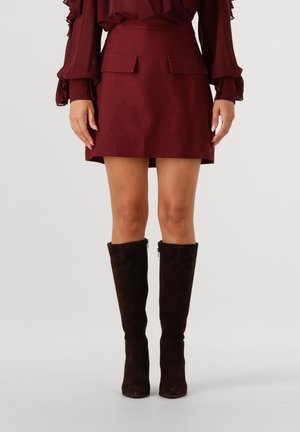 Burgundy mini skirt with front pockets, paired with knee-high black suede boots. The fabric appears smooth with a structured fit.