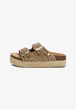 Sandalia de estilo trenzado de paja en color marrón con dos correas ajustables de metal con hebilla, plantilla de corcho y suela de yute texturizada. Diseño plano para mayor comodidad.