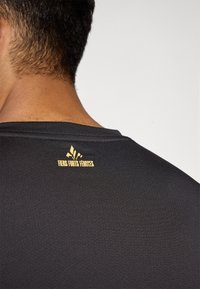 Sort atletisk skjorte med en glat overflade og rund halsudskæring. Guldtekst "Fiers Forts Fertes" og logo på ryggen.