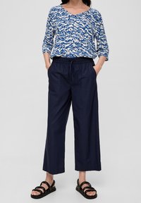 Top blu e bianco a fantasia con scollatura a V, abbinato a pantaloni larghi blu navy. Sandali neri con più cinturini completano l'outfit.