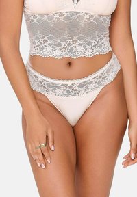 Set di bralette in pizzo e perizoma in beige chiaro. Presenta un delicato bordo in pizzo floreale sulla cintura e sull'orlo, con una base in tessuto liscio e lucido.