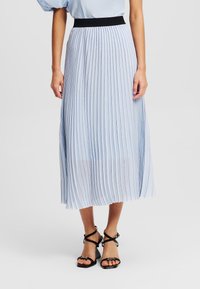 Jupe midi plissée bleu clair avec une taille élastique noire. Présente des rayures verticales et une texture fluide, complétée par des sandales noires à lanières.