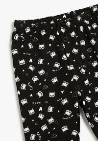 Leotard negro con un patrón repetido de rostros de gatos blancos, corazones y texto. Hecho de una tela suave con una cintura elástica.