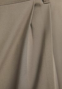 Tejido plisado en un color topo suave con una textura lisa. Presenta un brillo sutil y costuras limpias. Sin herrajes o acentos visibles.