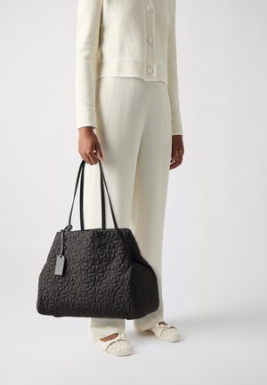Black quilted tote bag with double handles, featuring floral pattern and a small tag. Structured shape with soft texture.
