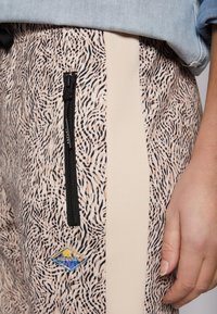 Mönstrade joggers med en beige elastisk sidpanel, ficka med dragkedja och en färgglad logopatch med svart, vitt och rosa design.