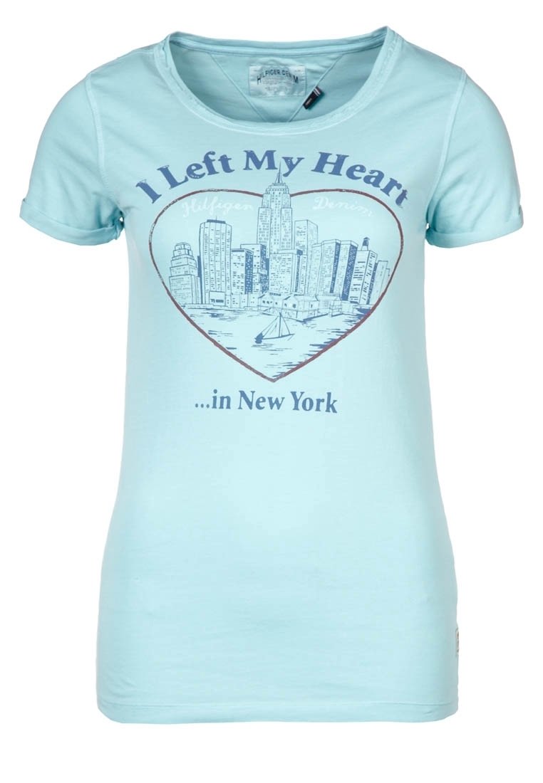 Camiseta de color azul claro con un horizonte de Nueva York en forma de corazón y el texto "Dejé mi corazón...en Nueva York" impreso en la parte frontal.