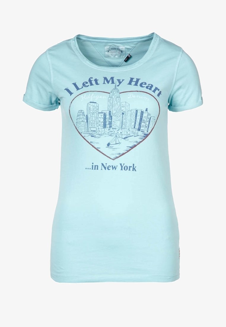 Camiseta de color azul claro con un horizonte de Nueva York en forma de corazón y el texto "Dejé mi corazón...en Nueva York" impreso en la parte frontal.