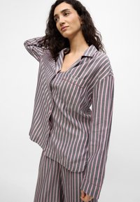 Conjunto de pijama a rayas grises y rosas hecho de tela suave, que incluye una camiseta de corte holgado con un bolsillo en el pecho y mangas largas, combinada con pantalones a juego.