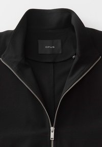 Black zip-up jacket with a high collar, smooth texture, silver zipper, and an interior label marked "OPUS." Clean design with minimal details.