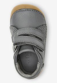 Grau Leder Schuh mit durchbrochenen Akzenten, zwei Klettverschlüssen und einer braunen Gummisohle. Das Innenleben zeigt eine weiche Fütterung und geprägte Größenangabe.