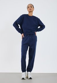 Navy blue cotton sweatshirt with crew neck and ribbed cuffs, paired with matching drawstring sweatpants and gray athletic shoes.