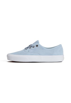 Lichtblauwe lage canvas sneaker met witte rubberen zool en metalen veterogen, weergegeven vanaf de zijkant op een witte achtergrond.