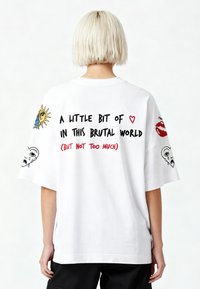 Balta didelė marškinė su spalvingų grafikų deriniu, įskaitant saulę, lūpas ir veidą, o nugaroje esantis tekstas yra paryškintais juodais ir raudonais rašmenimis.