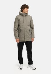 Gray textured hooded jacket with a front zip closure, side pockets, worn over black pants and white sneakers.