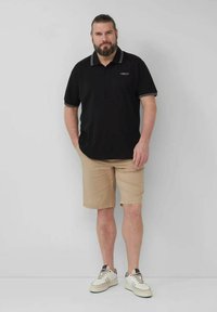 Schwarzes Poloshirt mit weißen Akzenten, beigen Shorts und weißen Sneakers. Das Poloshirt hat einen klassischen Kragen und ein Logo auf der Brust.