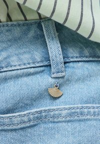 Blugi din denim albastru deschis cu un charm argintiu în formă de evantai atârnat de o buclă a curelei și o cămașă albă cu dungi negre deasupra.