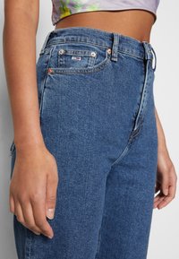 Jeans de mezclilla azul de cintura alta con un ajuste clásico, que cuentan con un diseño de cinco bolsillos, herrajes de cobre y sutiles detalles de costura.