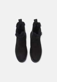 Musta mokkasukkaset kengät sisältävät turkisvuoratut kaulukset ja elastiset sivupaneelit helppoa pukemista varten. Pohja on teksturoitu pitävyyden vuoksi.