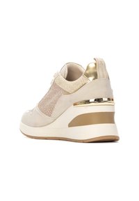 Zapatillas de cuña beige con malla perforada y detalles brillantes. Presentan un acento dorado alrededor del talón y una suela texturizada para un mejor agarre.