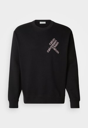 Black sweatshirt made of cotton, featuring a crew neckline and long sleeves. Notable light pink diagonal text logo on the front.