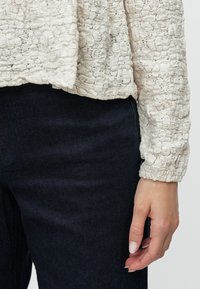 Top em tom marfim com uma textura subtil, padrão discreto, mangas longas e um corte relaxado, combinado com jeans de denim escuro.