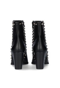 Botas de tobillo de cuero negro con un acabado texturizado, presentan tachuelas metálicas plateadas a lo largo de los lados y tacones gruesos y altos. Cierre de cremallera en la parte posterior.