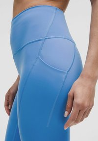 Nieco podwyższone, niebieskie legginsy sportowe wykonane z gładkiego, elastycznego materiału; mają detale wzdłuż szwów i elegancki krój, idealne do ćwiczeń.