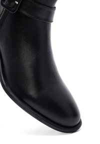 Bottine en cuir noir avec un embout pointu, une texture lisse et une fine sangle sur le dessus avec une boucle en argent.