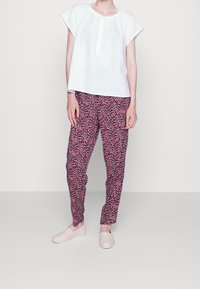 Biała, krótki rękaw, zapinana bluzka w połączeniu z różowymi spodniami w wzory. Lekki materiał, luźny krój oraz miękkie, jasne buty wsuwane.