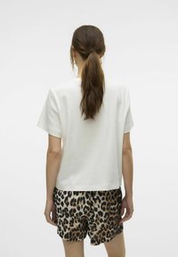 Witte katoenen t-shirt met korte mouwen, gecombineerd met shorts met een luipaardprint in verschillende bruin- en beigetinten, gezien vanaf de achterkant.