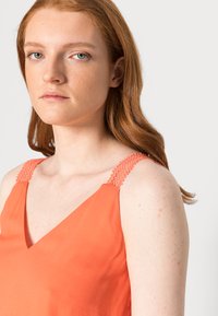 Top sem mangas cor de coral com decote em V e alças de malha texturizada. Tecido suave, corte descontraído e design minimalista.