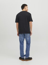 Schwarzes Baumwoll-T-Shirt mit kurzen Ärmeln, kombiniert mit hellblauen Jeans und schwarzen Slippers. Sichtbare Nähte an den Jeans.