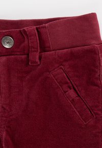 Burgunderfarbene Cordhose mit Knopfverschluss, gesteppten Akzenten und einem gerippten Bund, ausgestattet mit einer Seitentasche und weicher Textur.