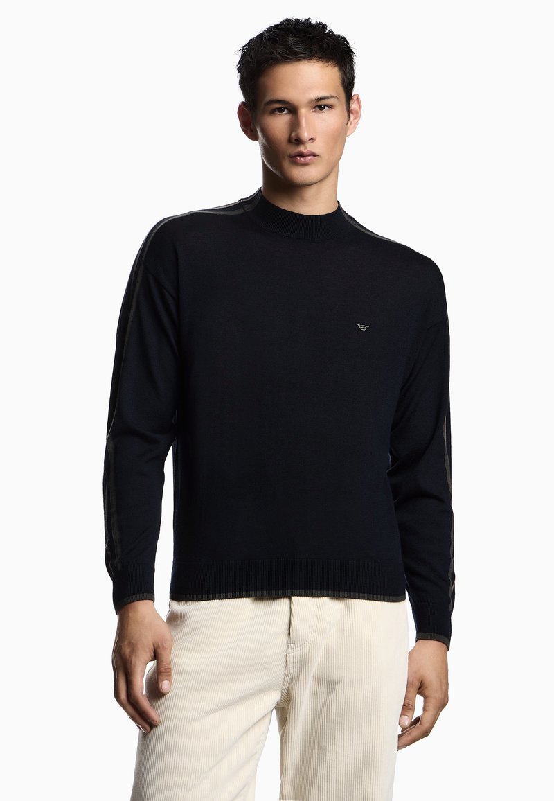 Maglione nero in maglia con collo alto. Presenta strisce laterali in contrasto e un piccolo logo sul petto. Texture morbida e design aderente.