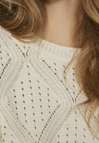 Biały sweter robiony na drutach, z teksturowanym wzorem w zygzaki i kształty rombów. Ściągaczowy dekolt oraz otwarta struktura dzianiny w całej powierzchni.