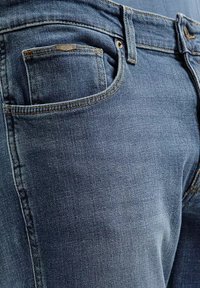 Jeans denim w ciemnoniebieskim odcieniu z klasycznym pięcio-kieszonkowym wzorem, z pomarańczowymi szwami oraz małym metalowym logo na przedniej kieszeni.