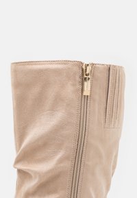 Stivale in finta suede beige con cerniera laterale in metallo dorato, dettagli di cuciture verticali e design superiore arricciato.