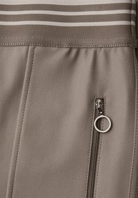 Beiger Stoff mit strukturierter Oberfläche, der horizontale Streifen in Braun- und Weißtönen sowie eine Reißverschlusstasche mit einem silbernen Ringzug hat.